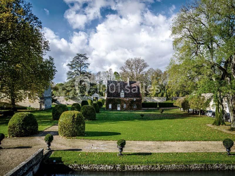 Maison entourée de pelouses et d'arbres dans un jardin paysager, sous un ciel partiellement nuageux.