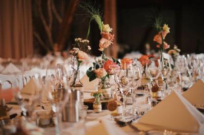Salle de réception décorée avec des tables rondes dressées, des fleurs colorées et un mur de briques apparentes.