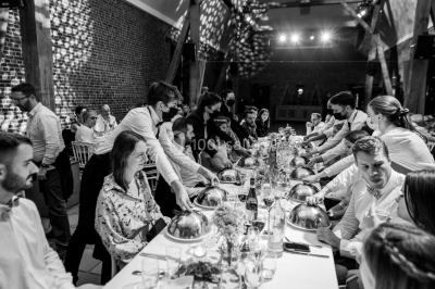Salle de réception décorée avec des tables rondes dressées, des fleurs colorées et un mur de briques apparentes.