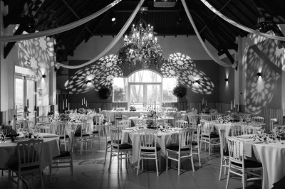 Salle de réception décorée avec des tables rondes dressées, des fleurs colorées et un mur de briques apparentes.