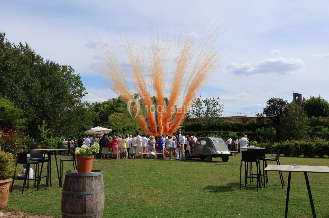 Un groupe de personnes rassemblées dans un jardin observe une explosion festive de fumée orange.