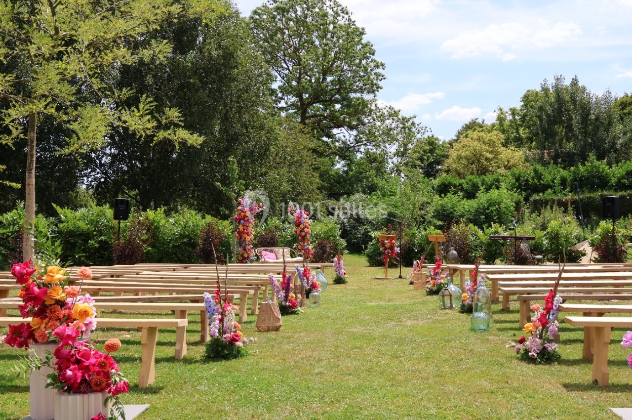 Allée centrale bordée de bancs en bois et de compositions florales colorées, dans un jardin verdoyant.