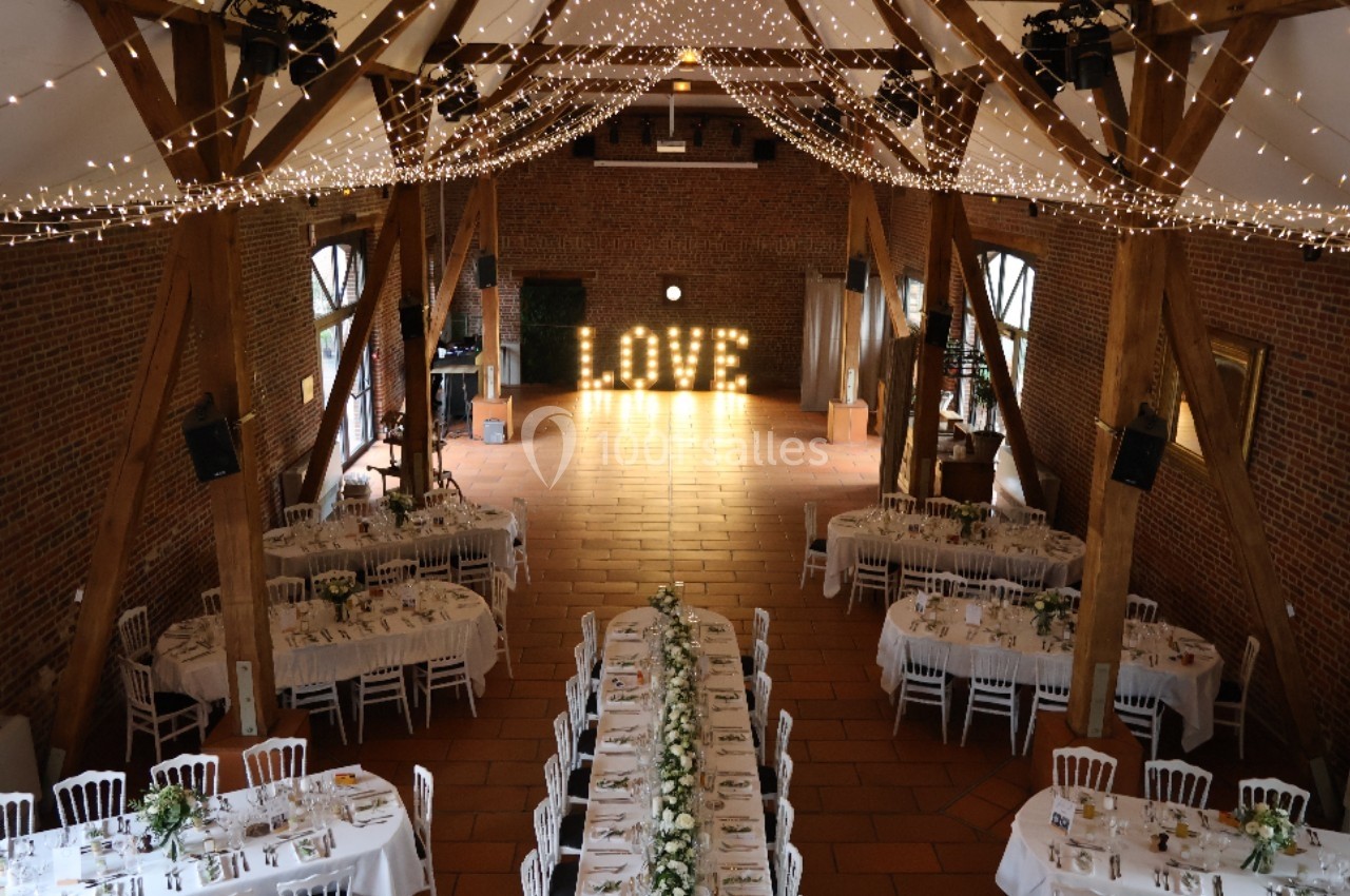 Salle de réception décorée avec guirlandes lumineuses, tables dressées et lettres lumineuses formant ’LOVE’.