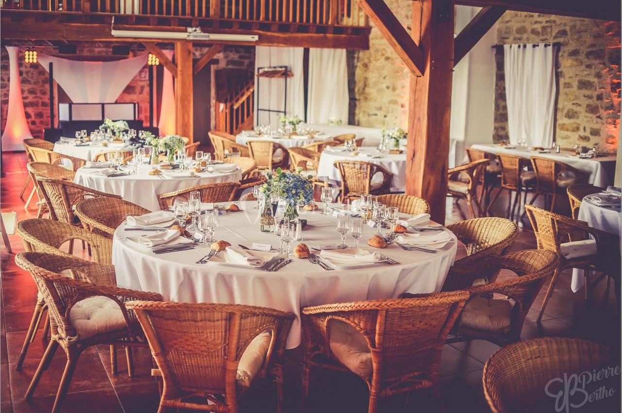 Salle de réception avec tables rondes dressées, nappes blanches, chaises en rotin et décoration florale.