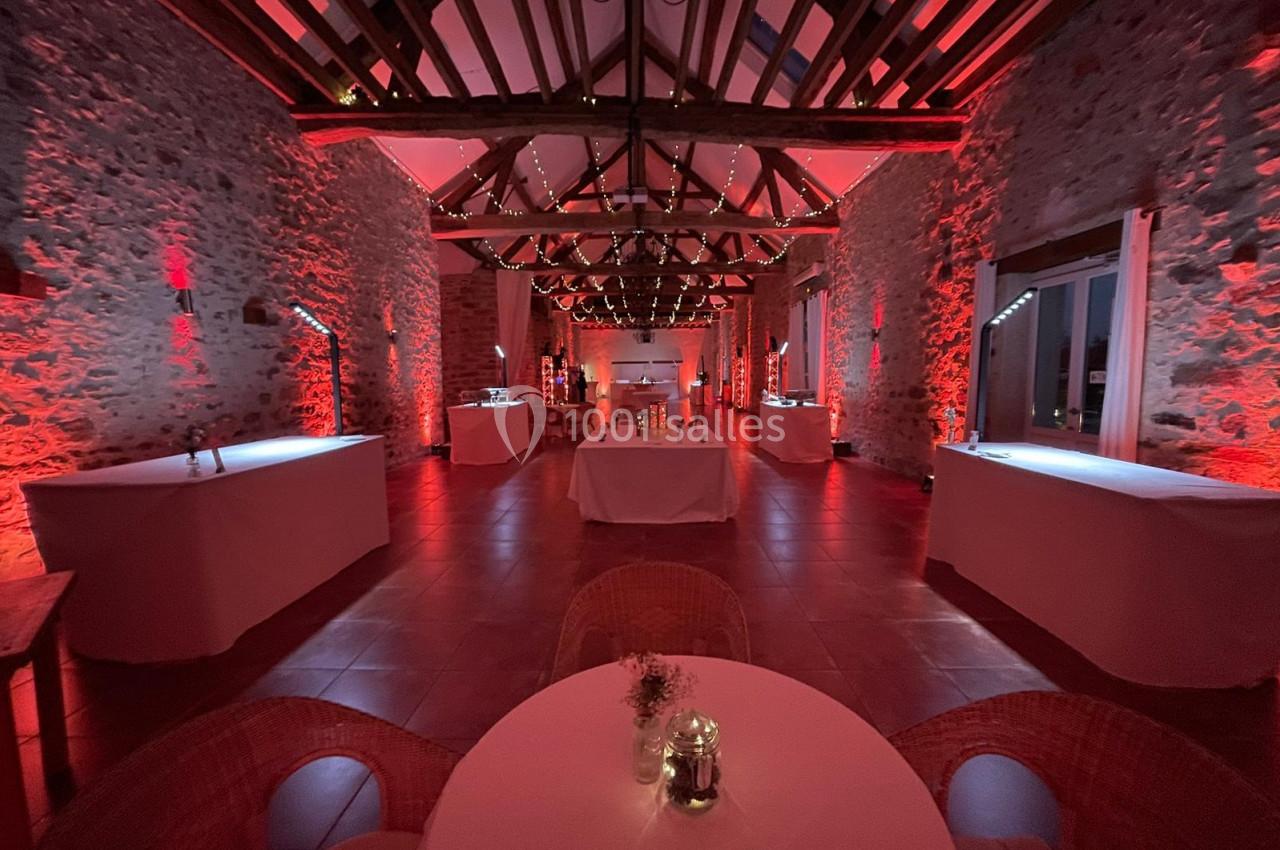 Salle en pierre avec poutres apparentes, éclairage rouge, tables décorées et ambiance chaleureuse.