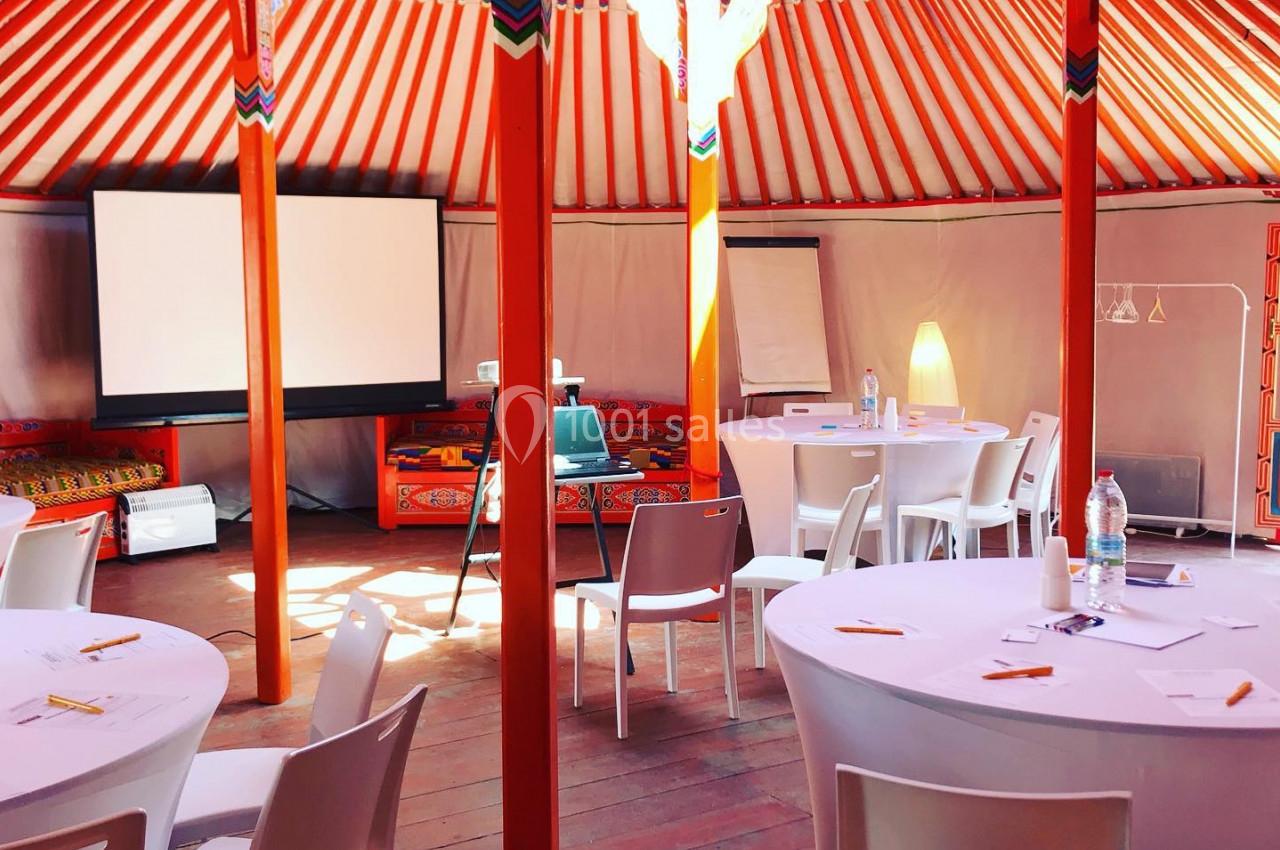 Intérieur d'une yourte aménagée en salle de réunion avec tables rondes, chaises blanches et matériel de présentation.