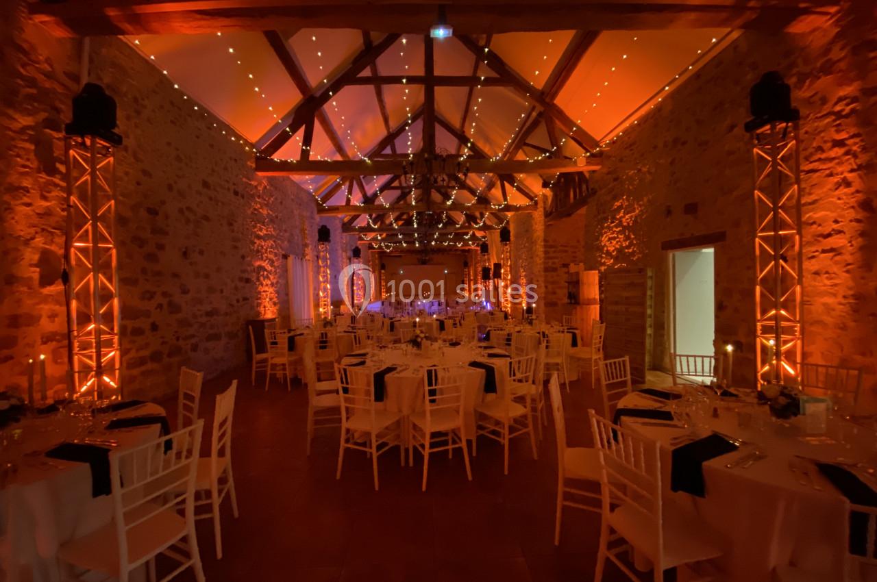 Salle de réception en pierre avec tables dressées, éclairage chaleureux et poutres apparentes au plafond.