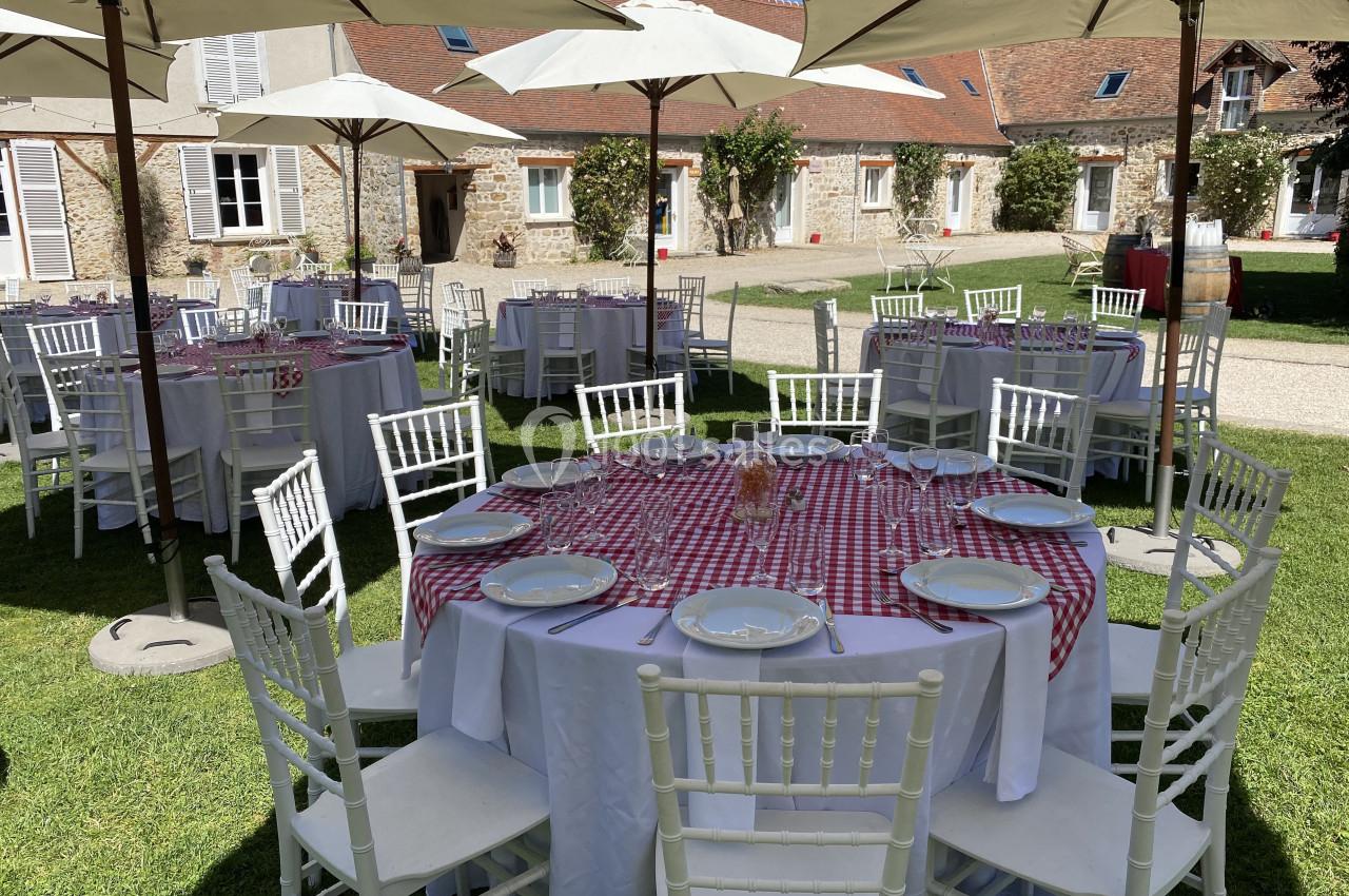 Tables rondes dressées avec nappes à carreaux rouges et blanches, disposées en extérieur sous des parasols.