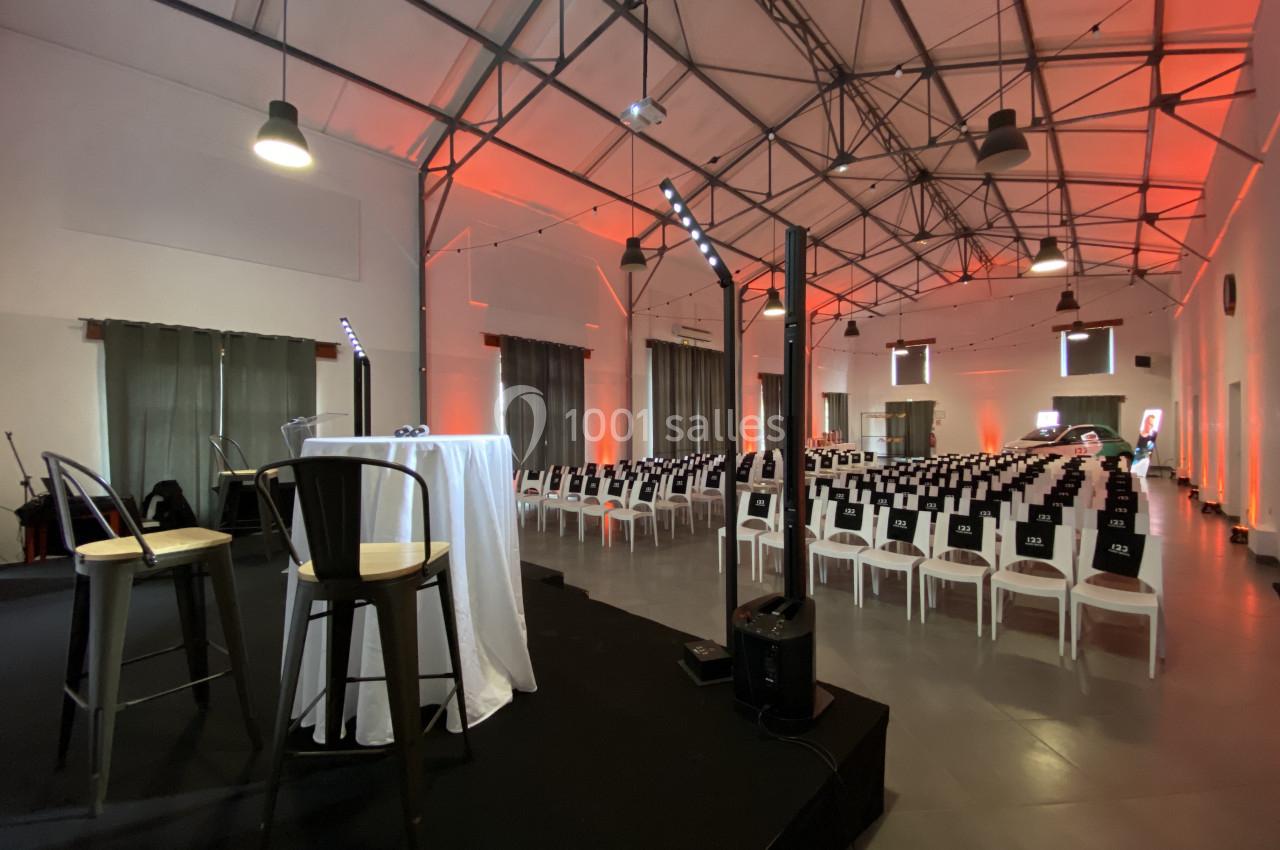 Salle de conférence avec chaises alignées, scène équipée de micros et éclairage tamisé orange.