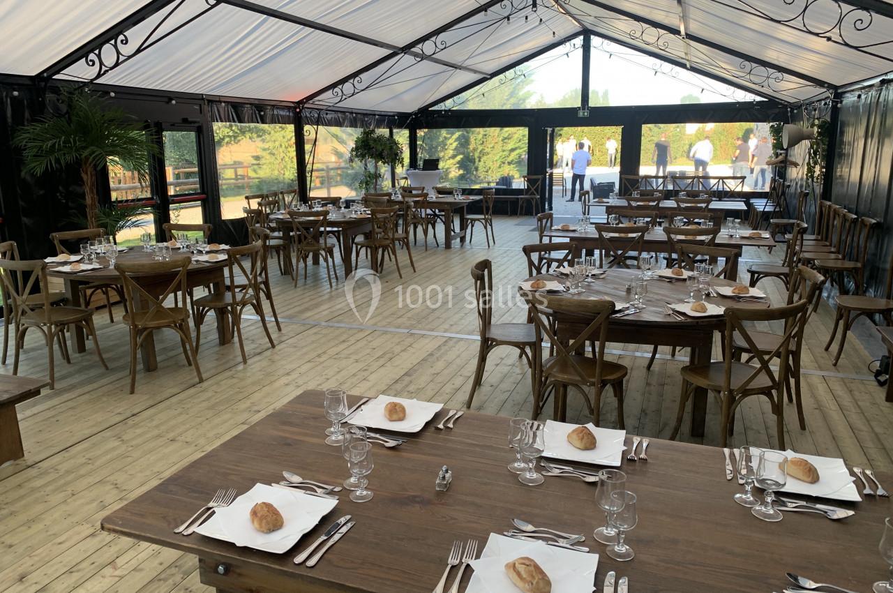 Salle de réception avec tables en bois dressées, couverts disposés et vue sur l'extérieur à travers des parois vitrées.