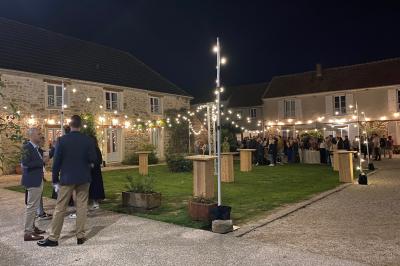Cour extérieure éclairée par des guirlandes lumineuses, avec des invités rassemblés près de tables hautes.