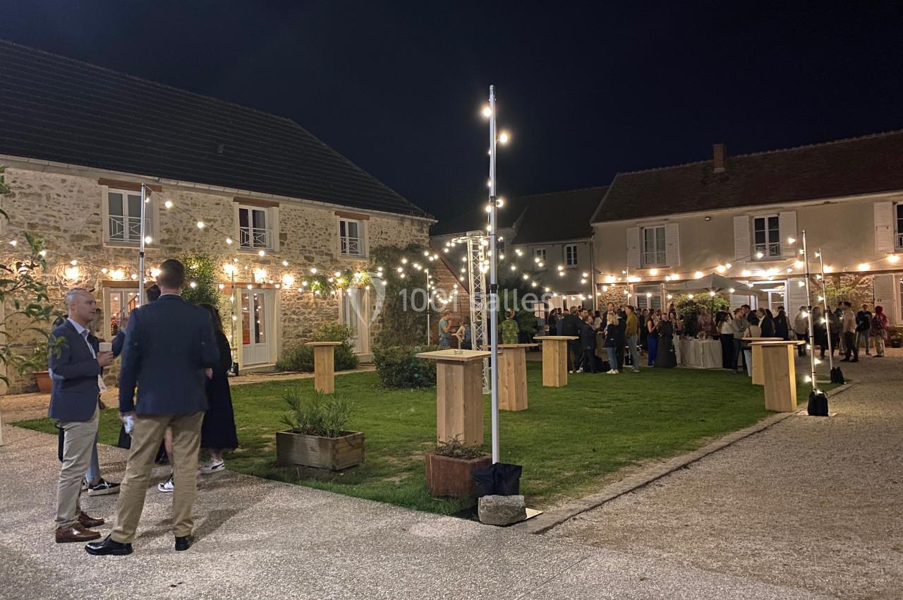 Cour extérieure éclairée par des guirlandes lumineuses, avec des invités rassemblés près de tables hautes.