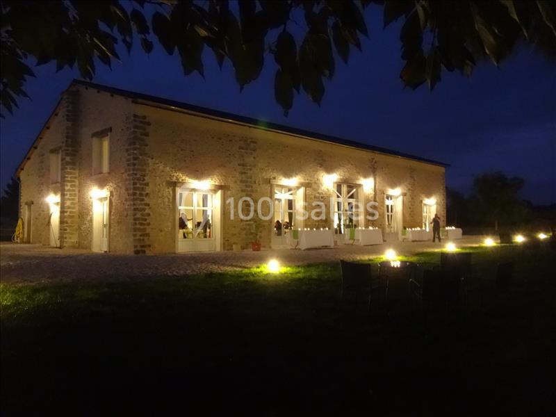 Bâtiment en pierre éclairé la nuit, avec de grandes fenêtres et un espace extérieur aménagé.