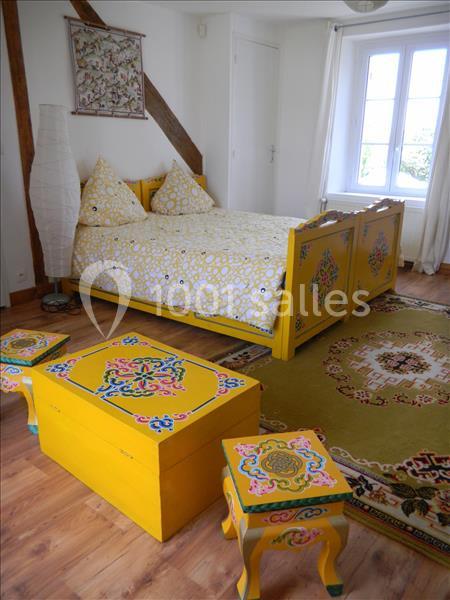 Chambre lumineuse avec lit et mobilier en bois peint jaune à motifs colorés, tapis et grande fenêtre.