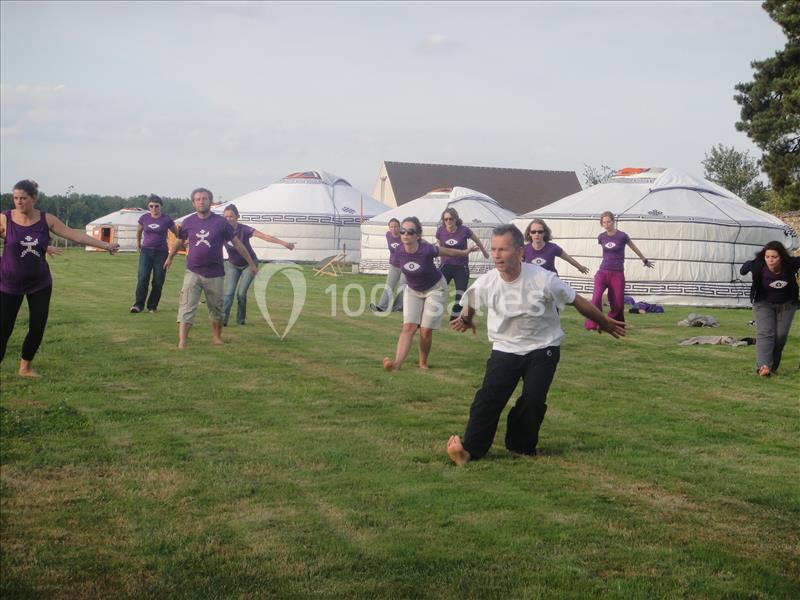 Un groupe de personnes pratique des exercices en plein air sur une pelouse, avec des yourtes blanches en arrière-plan.