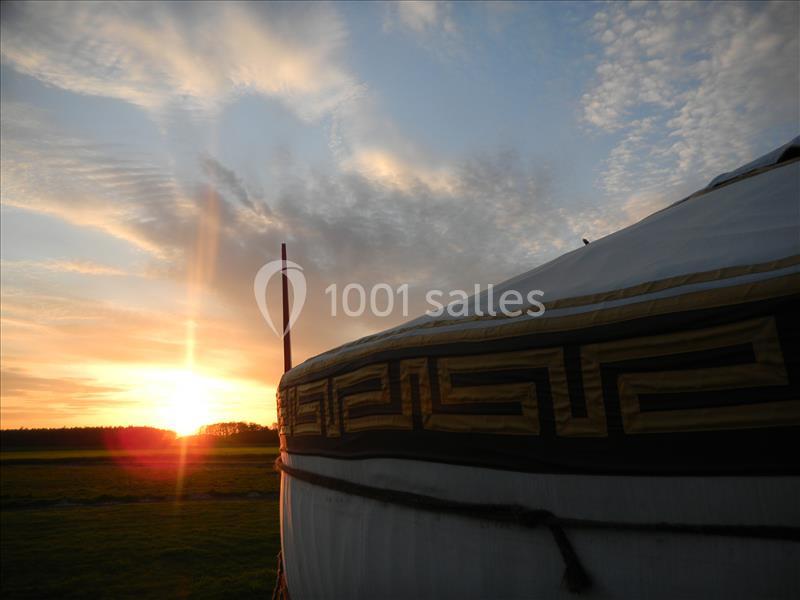 Une yourte blanche ornée de motifs géométriques, éclairée par un coucher de soleil sur un paysage champêtre.