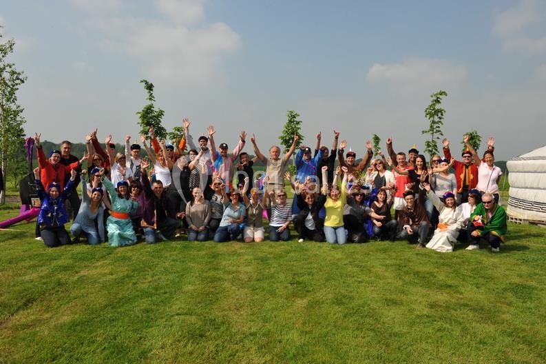 Un groupe de personnes souriantes posant en plein air sur une pelouse, levant les bras dans une ambiance festive.