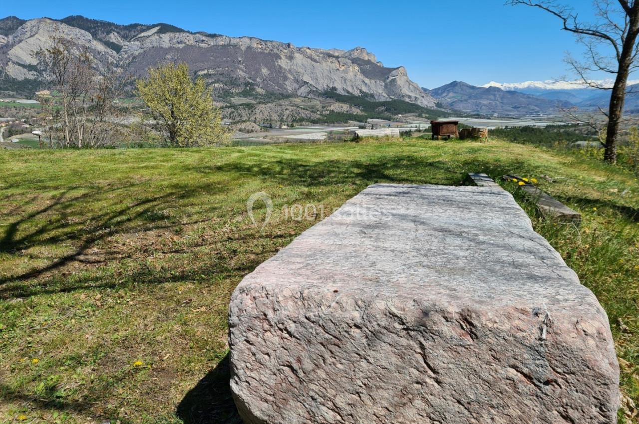 Bloc de pierre rectangulaire sur une pelouse avec vue sur des montagnes et un ciel dégagé en arrière-plan.