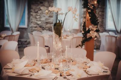 Table en pierre sous une voûte en pierre, avec un pot de fleurs et des outils anciens accrochés au mur.