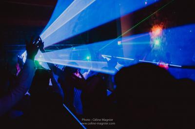 Table en pierre sous une voûte en pierre, avec un pot de fleurs et des outils anciens accrochés au mur.