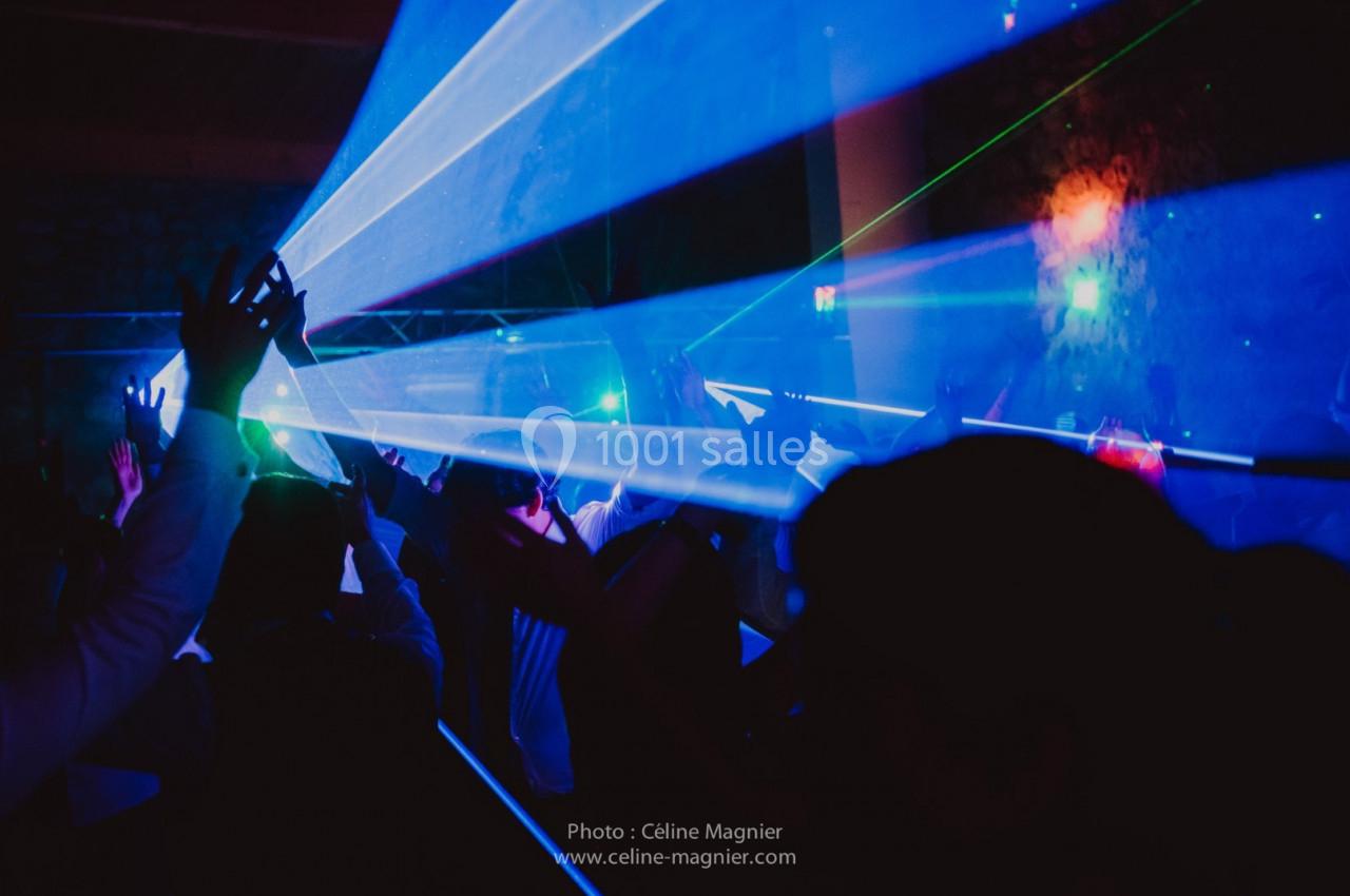 Des faisceaux lumineux bleus traversent une foule dansante dans une ambiance sombre et festive.