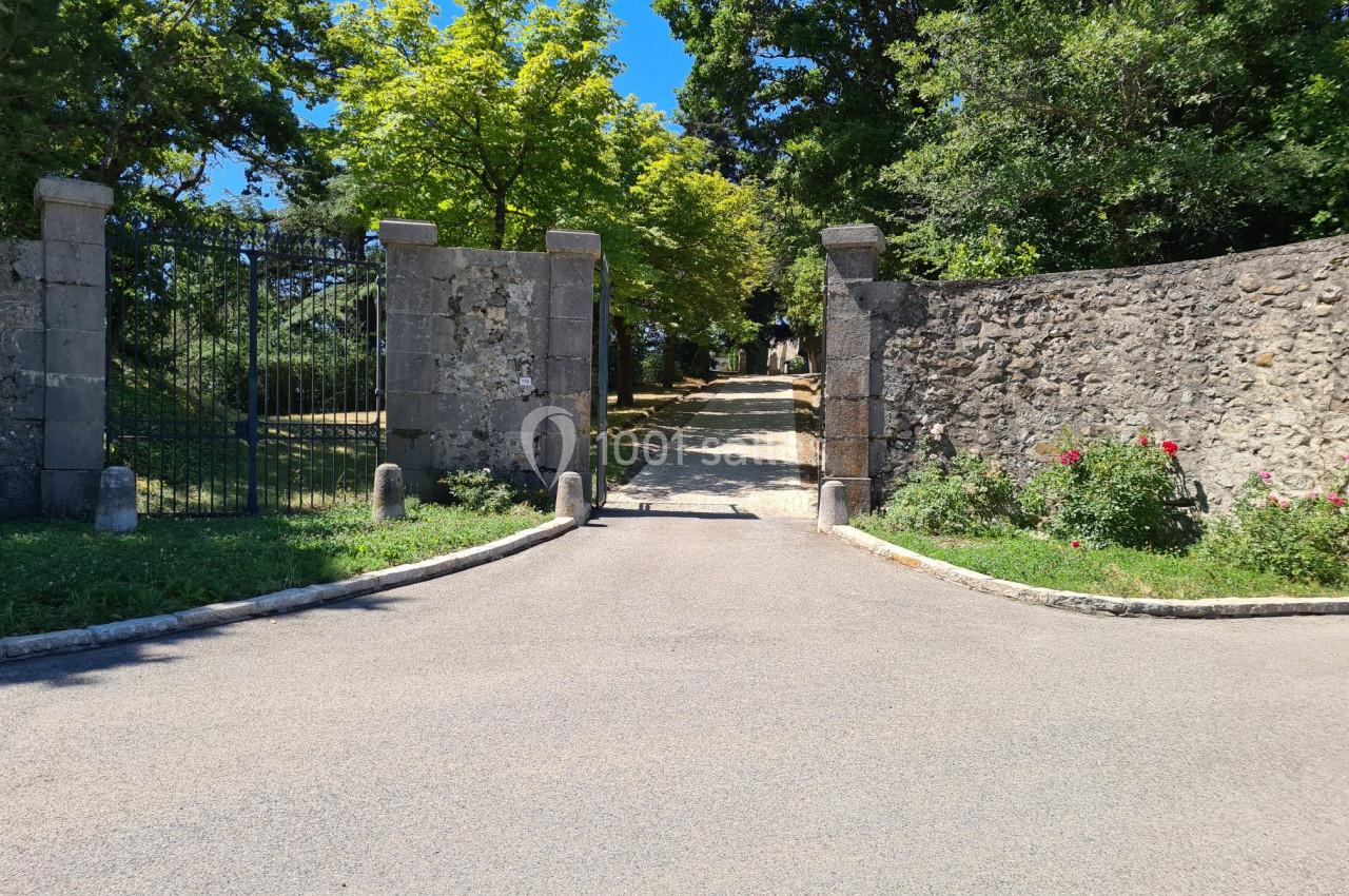 Entrée d'un chemin bordé de murs en pierre et de végétation, avec un portail ouvert sous un ciel dégagé.