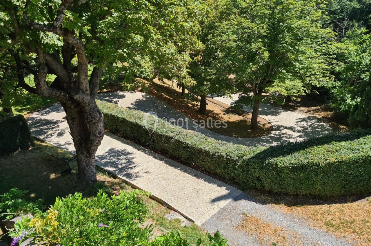Allée pavée bordée de haies et d'arbres dans un jardin ensoleillé, vue depuis une hauteur.