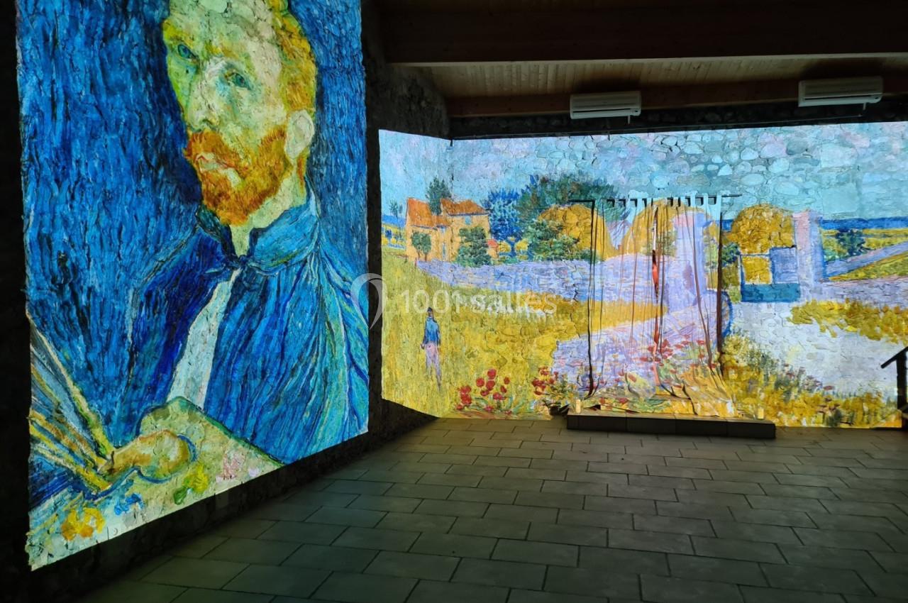 Projection immersive de peintures de Van Gogh sur les murs d'une salle sombre avec un sol en dalles grises.