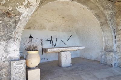 Table en pierre sous une voûte en pierre, avec un pot de fleurs et des outils anciens accrochés au mur.