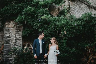 Table en pierre sous une voûte en pierre, avec un pot de fleurs et des outils anciens accrochés au mur.