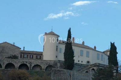 Table en pierre sous une voûte en pierre, avec un pot de fleurs et des outils anciens accrochés au mur.