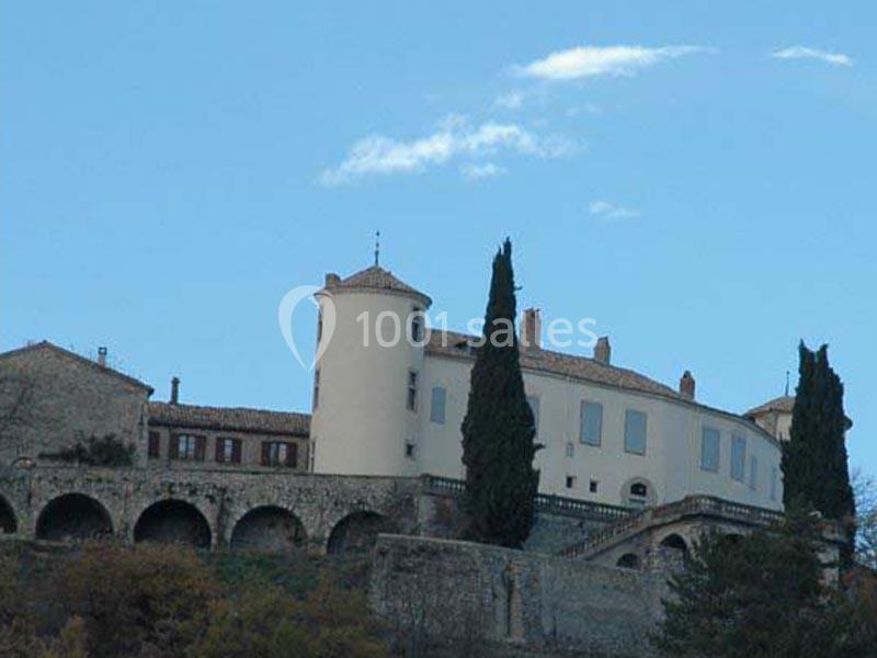 Château blanc avec tours et cyprès, perché sur une colline avec un ciel bleu en arrière-plan.