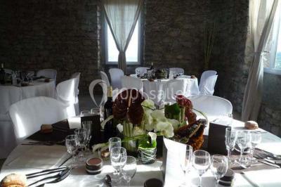 Table en pierre sous une voûte en pierre, avec un pot de fleurs et des outils anciens accrochés au mur.