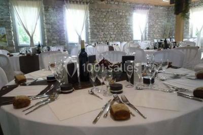 Table en pierre sous une voûte en pierre, avec un pot de fleurs et des outils anciens accrochés au mur.