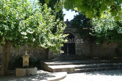 Table en pierre sous une voûte en pierre, avec un pot de fleurs et des outils anciens accrochés au mur.
