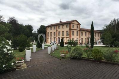 Couloir avec parquet en bois, murs verts décorés, table avec cadres et bougies, et rideaux verts aux fenêtres.