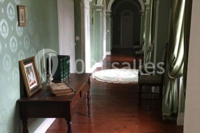 Couloir avec parquet en bois, murs verts décorés, table avec cadres et bougies, et rideaux verts aux fenêtres.