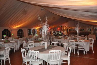 Couloir avec parquet en bois, murs verts décorés, table avec cadres et bougies, et rideaux verts aux fenêtres.
