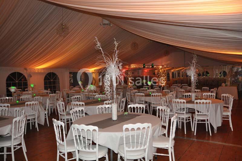 Salle de réception décorée avec des tables rondes, nappes blanches, chaises assorties et éclairage chaleureux.