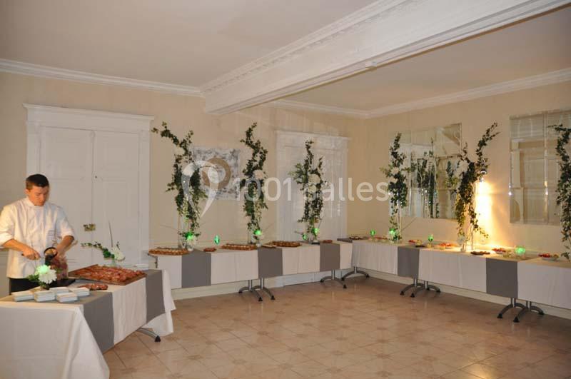 Un chef prépare un buffet dans une salle décorée de plantes et de guirlandes lumineuses, avec des tables garnies de plats.