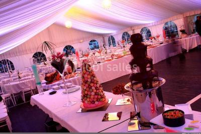 Couloir avec parquet en bois, murs verts décorés, table avec cadres et bougies, et rideaux verts aux fenêtres.