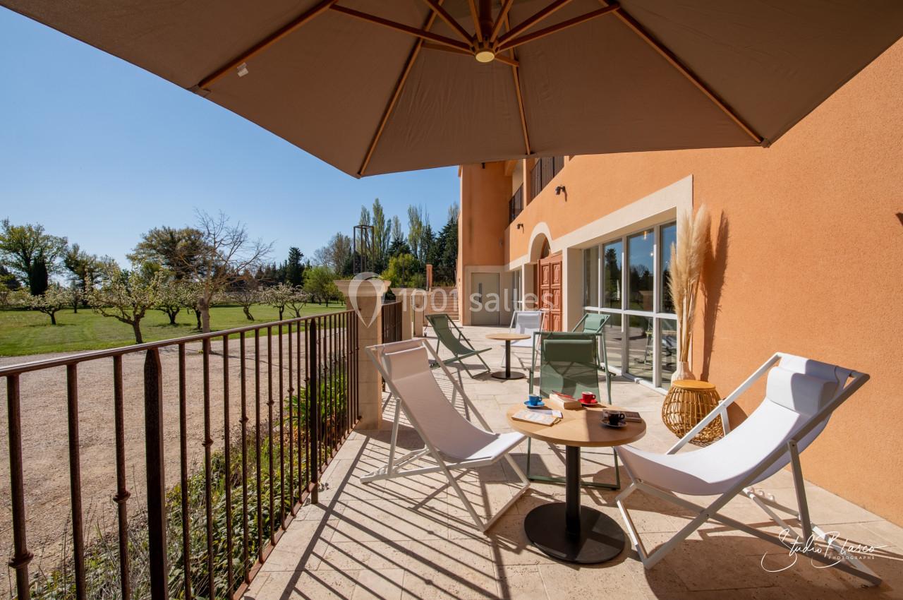 Terrasse ensoleillée avec chaises longues, table basse et parasol, donnant sur un jardin arboré.