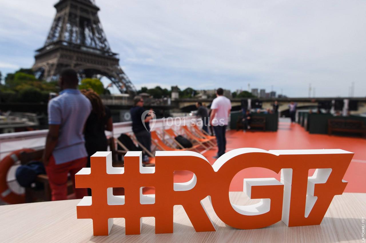Sculpture orange ’#RG17’ sur une table, avec la Tour Eiffel et des passants en arrière-plan.