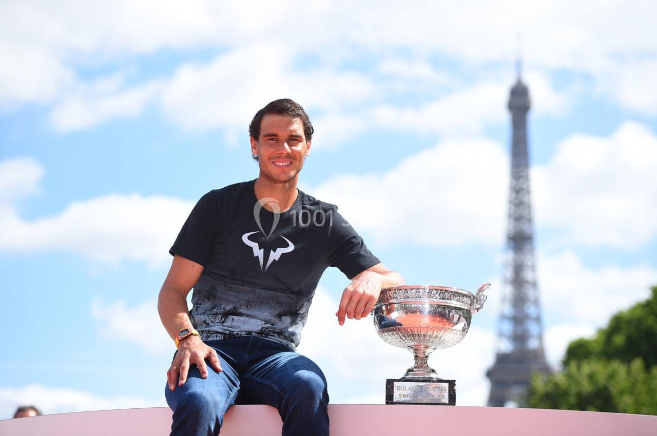 Un homme assis à l'extérieur avec un trophée en argent, la tour Eiffel visible en arrière-plan.