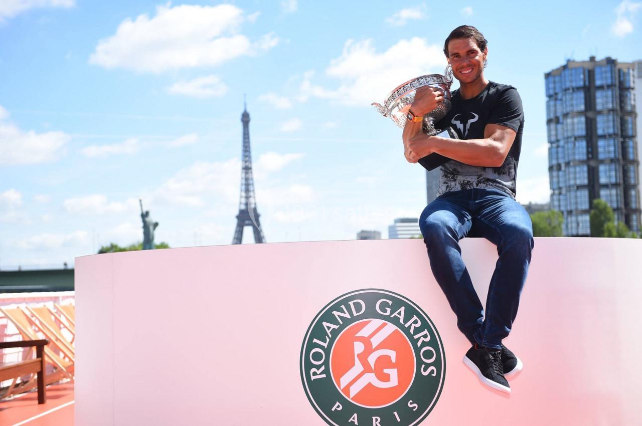 Un homme assis sur un podium Roland-Garros tenant un trophée, avec la Tour Eiffel en arrière-plan.