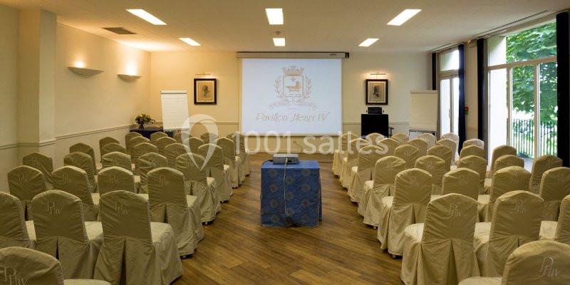 Salle de conférence lumineuse avec des chaises alignées, un projecteur, un écran et des tableaux de présentation.