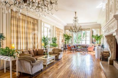 Deux tables de massage recouvertes de draps beiges, avec une vue sur un paysage urbain et verdoyant à travers une fenêtre.