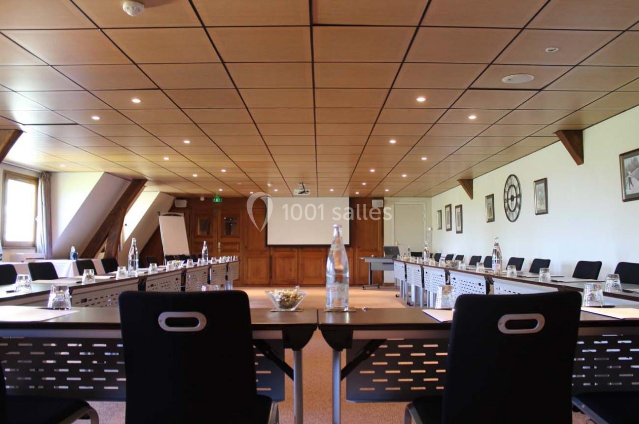 Salle de réunion lumineuse avec table en U, chaises noires, bouteilles d'eau et écran de projection au fond.