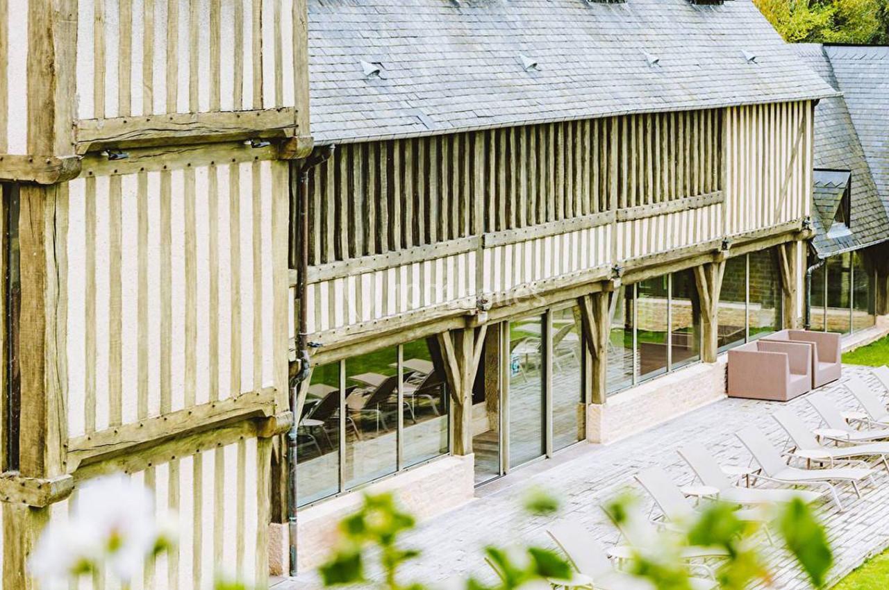 Façade en colombages d'un bâtiment avec terrasse en bois, chaises longues et baies vitrées donnant sur un espace vert.