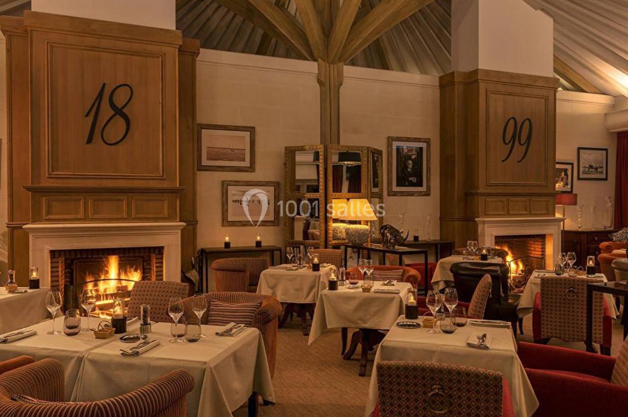 Salle de restaurant élégante avec tables dressées, cheminées allumées et éclairage chaleureux.
